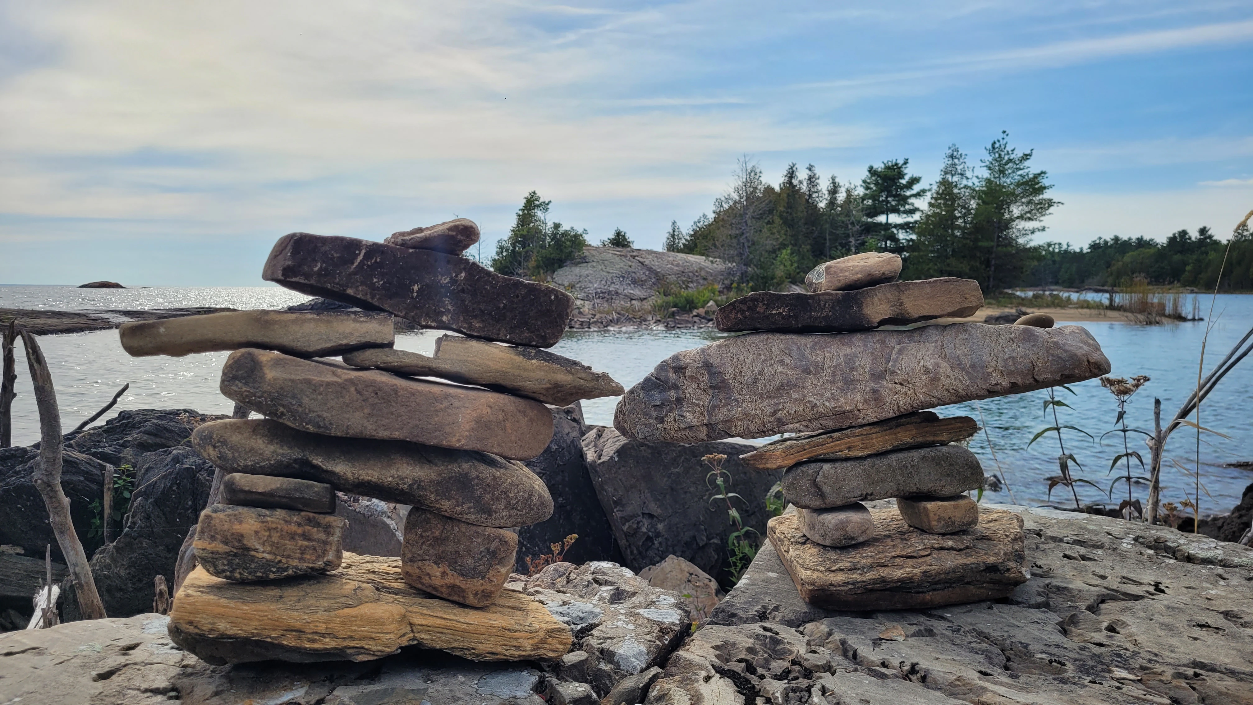 Two inukshuks on an island in the north channel overlooking other islands with trees and the sea and sky